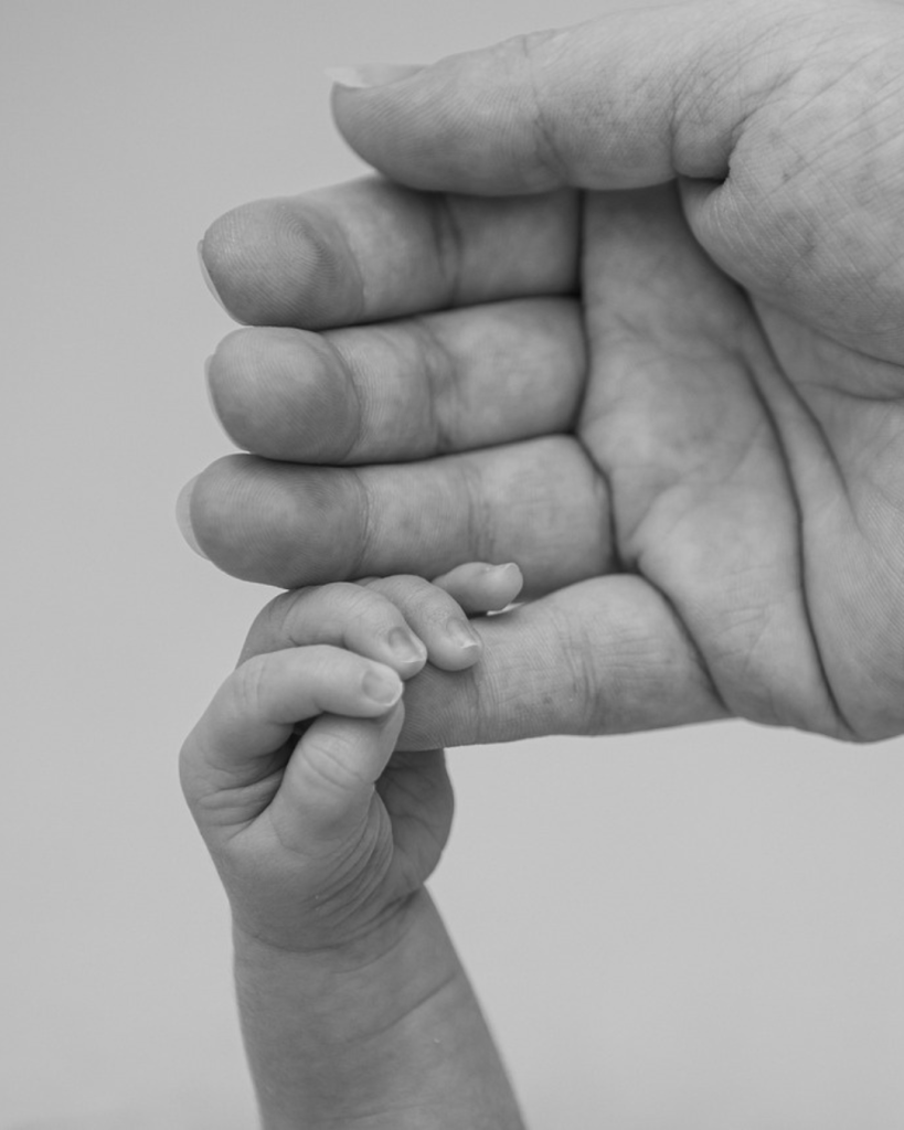 Une main d'adulte tenant la main d'un bébé. Cela fait penser à la généalogie.