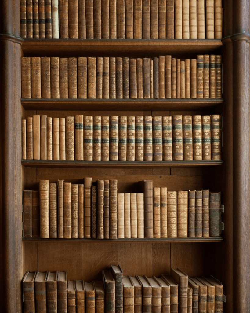 Des étagères d'une bibliothèque, avec des livres anciens. Ils ressemblent à des livres qu'on pourrait utiliser en généalogie.